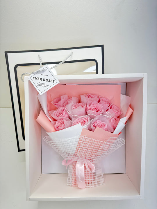 Bouquet of pink roses in a decorative box with a white ribbon.