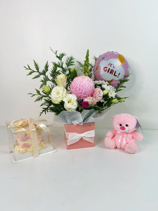 A gift set including a box of flowers with pink and white blossoms, a pink teddy bear, and a balloon with the message 'it's a girl'.
