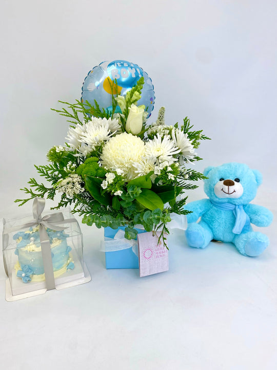 A gift set including a blue box, a white floral arrangement, a blue teddy bear, and a balloon with 'It is a boy' written on it.