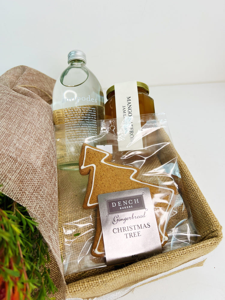Gift basket with gingerbread Christmas tree, bottle of water, and jar of jam on a white background