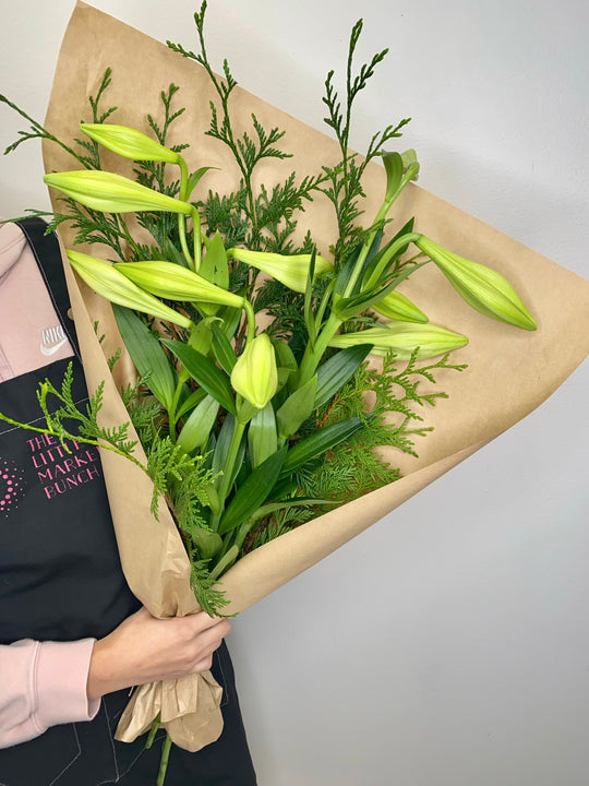 This image shows a fresh bouquet of unopened Christmas lilies, paired with lush green foliage and wrapped in natural kraft paper. shot by The Little Market Bunch, Melbourne.