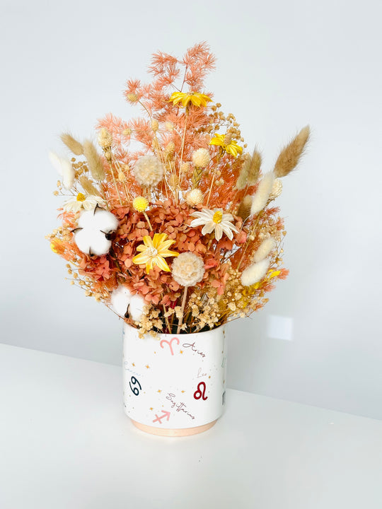
                  
                    Dried flower arrangement in a white vase with zodiac symbols on a light gray background
                  
                