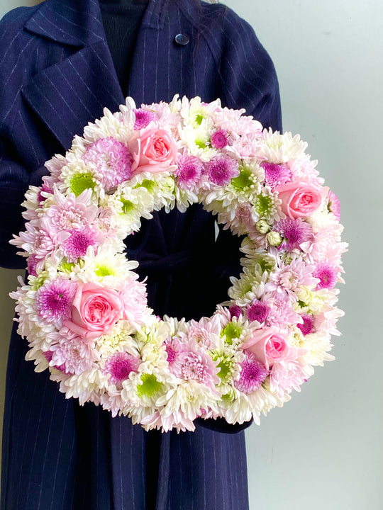 
                  
                    Floral wreath with pink and white flowers held by a person wearing a dark blue coat.
                  
                