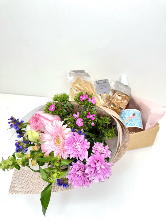 
                  
                    A beautifully arranged gift set featuring a bouquet of pink and purple flowers including gerbera, roses, and chrysanthemums, paired with a bottle of Solara Organic Rosé and a selection of packaged gourmet snacks in a Small hessian box. Shot by The Little Market Bunch, Melbourne.
                  
                