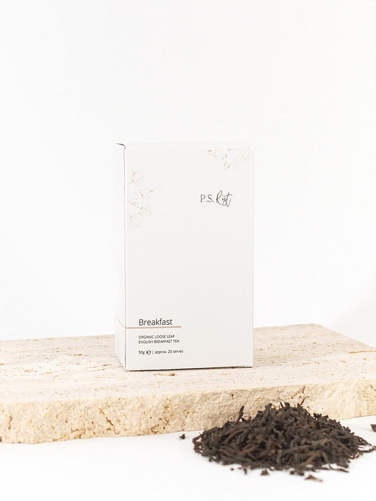 
                  
                    Tea packaging labeled 'Breakfast' on a wooden surface with loose tea leaves.
                  
                