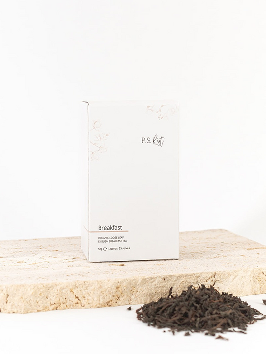 
                  
                    Tea packaging labeled 'Breakfast' on a wooden surface with loose tea leaves.
                  
                