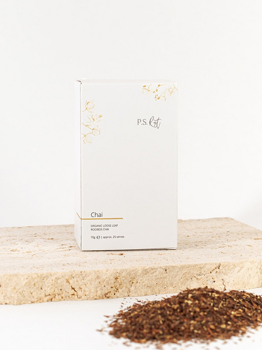 
                  
                    White box of P.S. Chai tea on a wooden surface with scattered tea leaves.
                  
                