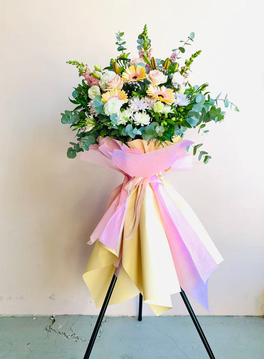Bouquet of flowers wrapped in pastel ribbons on a stand against a plain background
