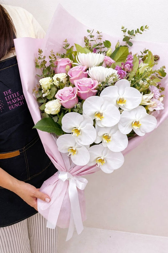 
                  
                    Bouquet of flowers with white orchids and pink roses held by a person wearing an apron.
                  
                