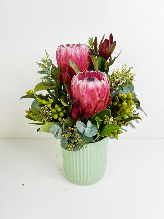 Floral arrangement with pink protea flowers in a green vase on a white background