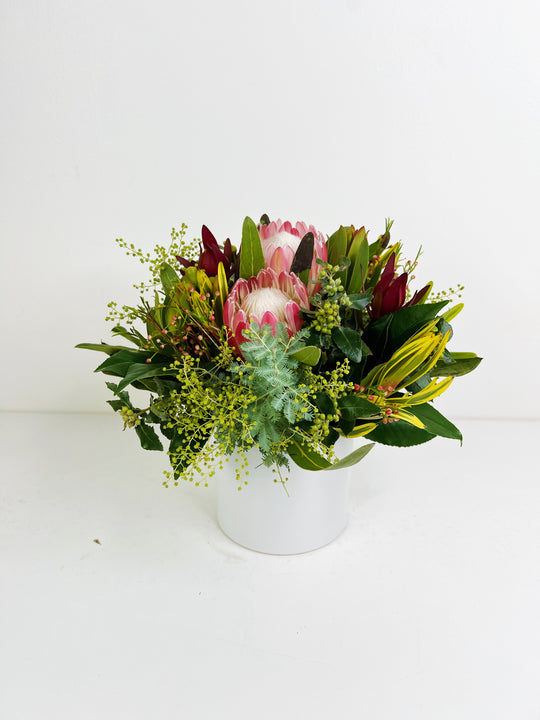 Floral arrangement with a pink protea in a white vase on a white background