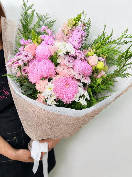 
                  
                    Bouquet of pink and white flowers with greenery held by a person against a neutral background
                  
                