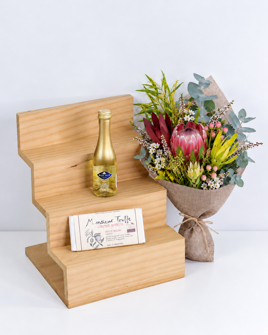 
                  
                    Bouquet of flowers, Gold leaf sparkling wine , and a chocolate on a wooden stand with a white background
                  
                