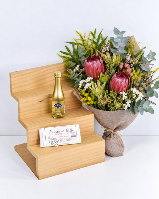 
                  
                    Bouquet of flowers, Gold leaf sparkling wine , and a chocolate on a wooden stand with a white background
                  
                