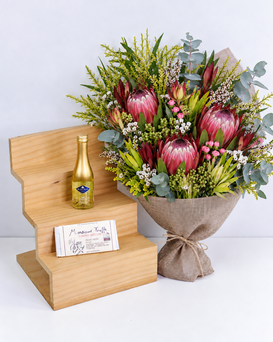 
                  
                    Bouquet of flowers, Gold leaf sparkling wine , and a chocolate on a wooden stand with a white background
                  
                