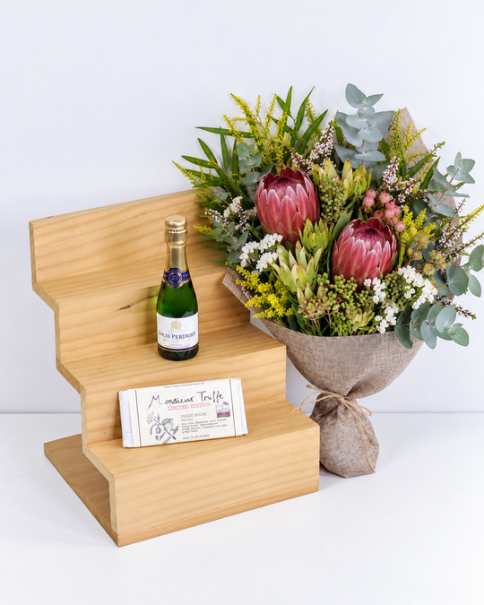 Bouquet of flowers, French sparkling wine , and a chocolate on a wooden stand with a white background