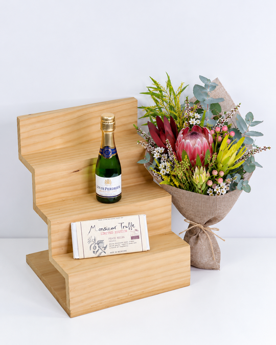 Bouquet of flowers, French sparkling wine , and a chocolate on a wooden stand with a white background
