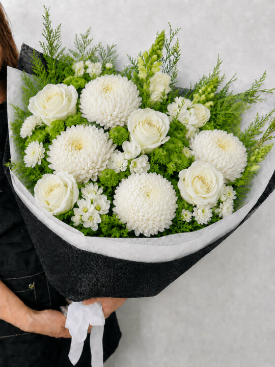 
                  
                    Bouquet of white flowers with greenery held by a person against a light background
                  
                