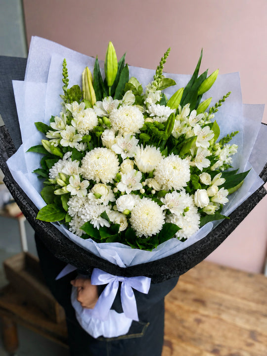 
                  
                    Bouquet of white flowers wrapped in black paper with a white ribbon.
                  
                