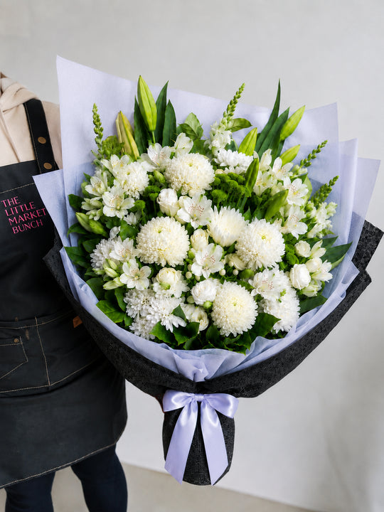 
                  
                    Bouquet of white flowers with greenery held by a person wearing an apron.
                  
                
