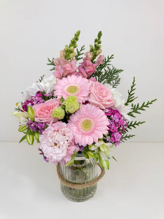 
                  
                    Bouquet of pink, purple, and white flowers in a glass vase on a light background
                  
                