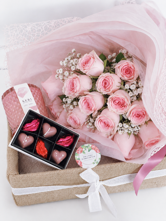A gift box containing a pink rose bouquet, six packs of chocolate hearts, and a fragrant premium candle.